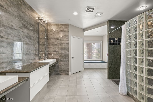 bathroom with tile walls, tile patterned flooring, a washtub, and vanity