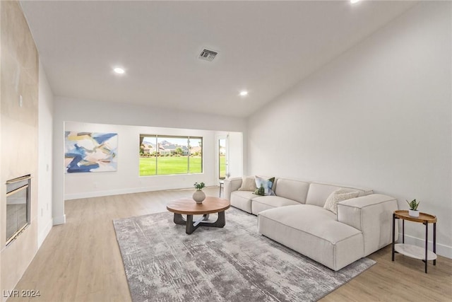 living room with a glass covered fireplace, visible vents, lofted ceiling, and wood finished floors