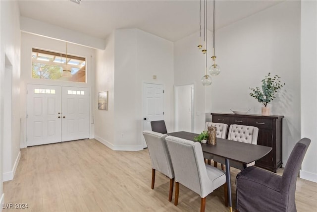 dining space featuring a towering ceiling, baseboards, and light wood finished floors