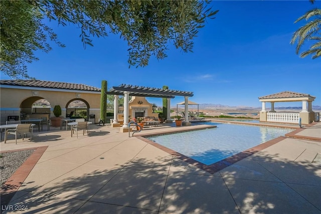 pool featuring an outdoor fireplace, a gazebo, a patio area, a mountain view, and a pergola