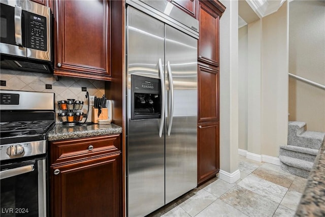 kitchen featuring reddish brown cabinets, stainless steel appliances, decorative backsplash, ornamental molding, and dark stone countertops