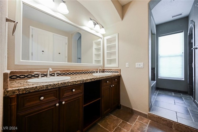 bathroom with stone tile flooring, double vanity, baseboards, and a sink