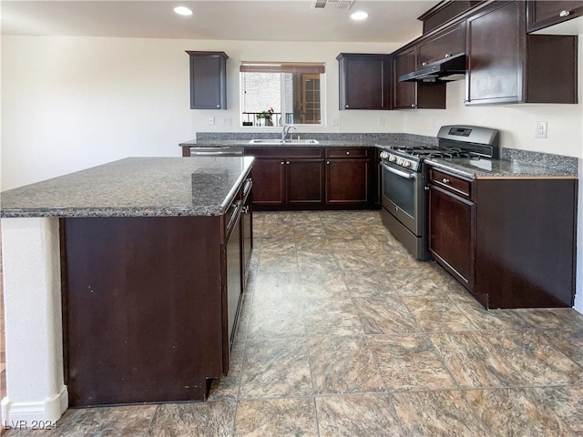 kitchen with gas stove, sink, dark stone counters, a kitchen island, and dark brown cabinets