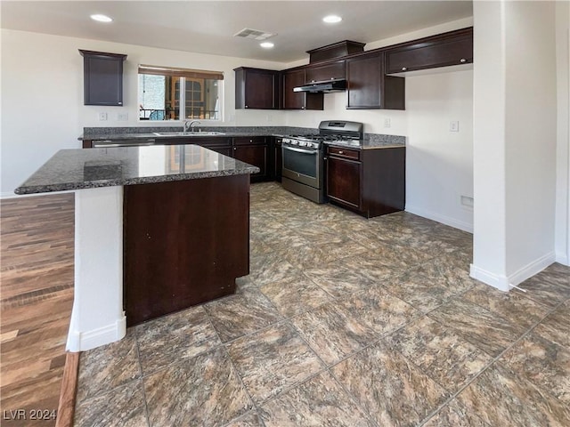 kitchen featuring gas range, a center island, dark brown cabinetry, sink, and dark stone counters