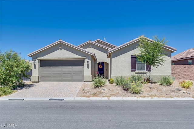 view of front facade featuring decorative driveway, an attached garage, a tile roof, and stucco siding