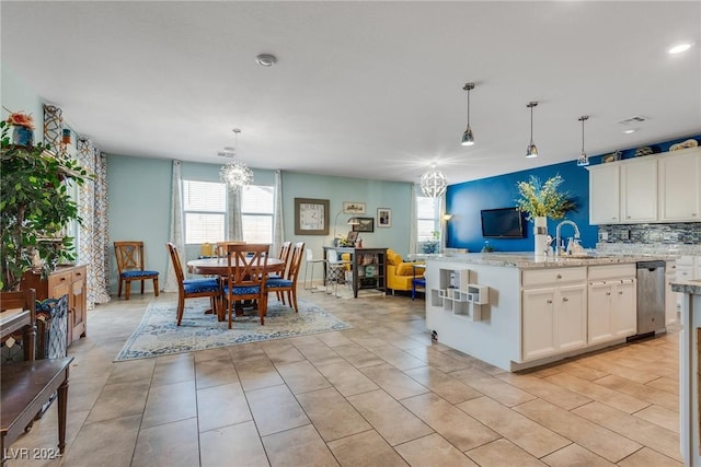 kitchen with light stone counters, open floor plan, white cabinetry, pendant lighting, and a sink