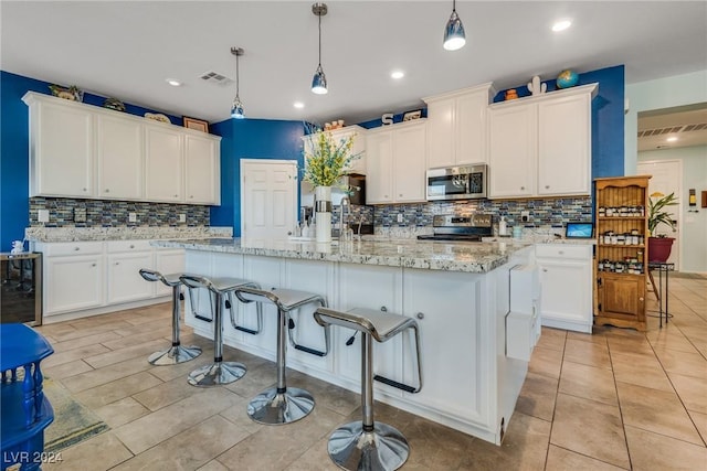 kitchen featuring visible vents, white cabinets, appliances with stainless steel finishes, an island with sink, and decorative light fixtures