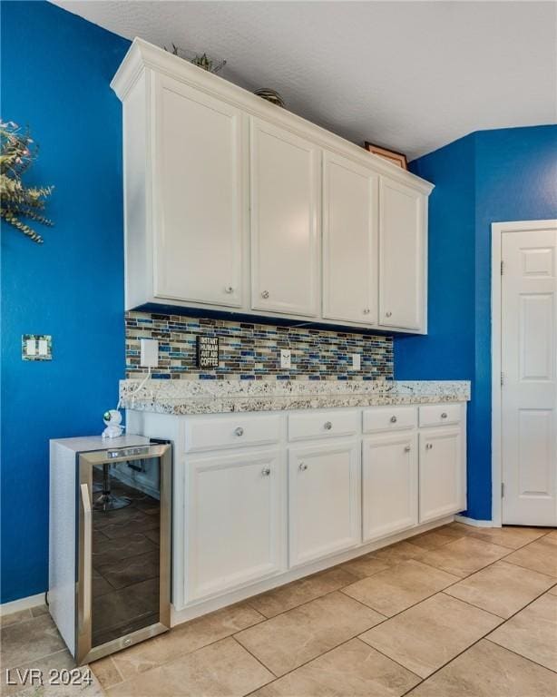 kitchen featuring wine cooler, light tile patterned flooring, white cabinets, backsplash, and light stone countertops