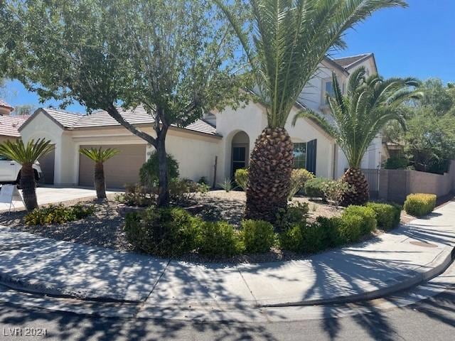 view of front facade featuring a tile roof, stucco siding, concrete driveway, an attached garage, and fence