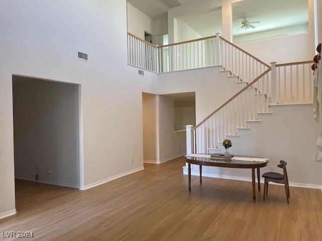 stairs featuring a towering ceiling, wood-type flooring, and ceiling fan