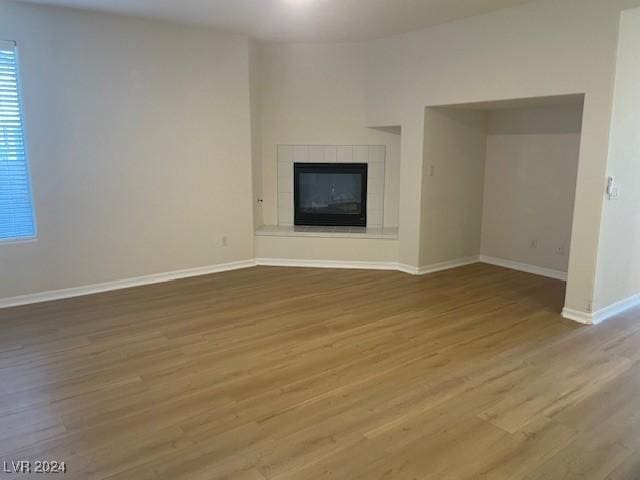 unfurnished living room featuring a tile fireplace, wood finished floors, and baseboards