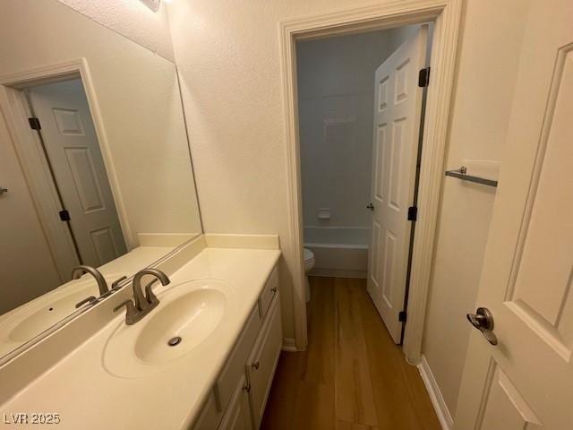 bathroom featuring vanity, wood finished floors, toilet, and a washtub