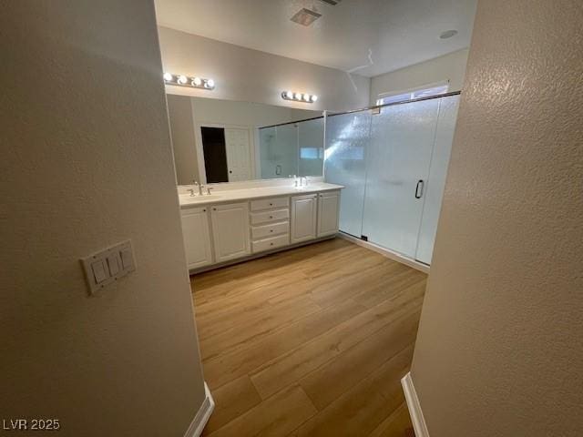 bathroom featuring a textured wall, wood finished floors, a sink, double vanity, and a stall shower