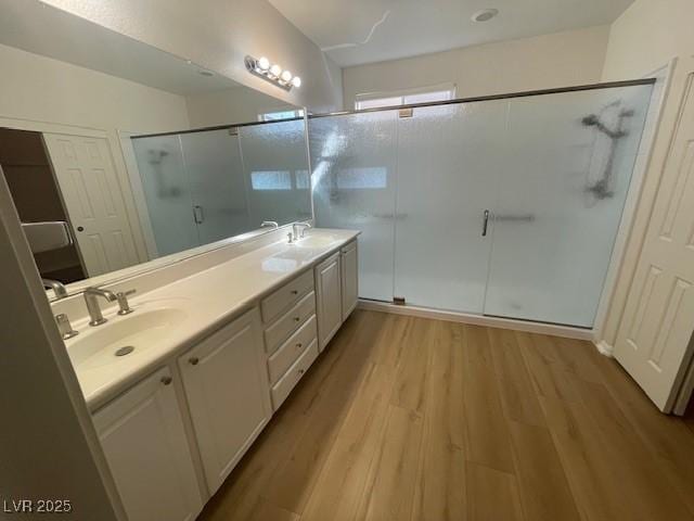 full bath with double vanity, wood finished floors, a sink, and a shower stall