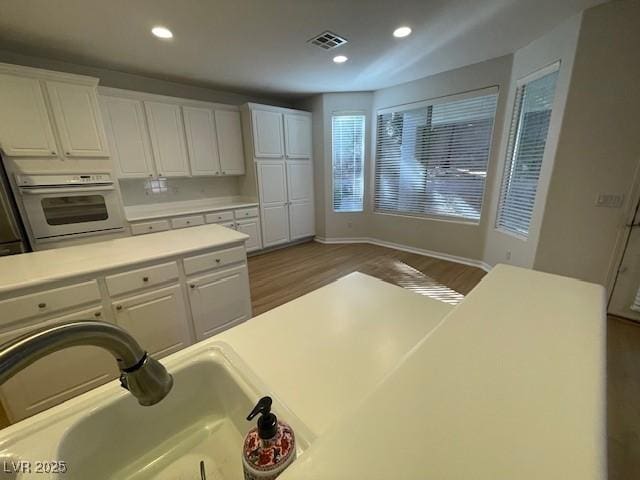 kitchen with wall oven, light countertops, white cabinets, and visible vents