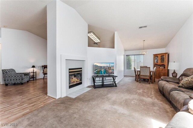 living room with an inviting chandelier, light hardwood / wood-style flooring, a tiled fireplace, and lofted ceiling