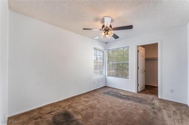 unfurnished bedroom with dark carpet, a walk in closet, a closet, and a textured ceiling