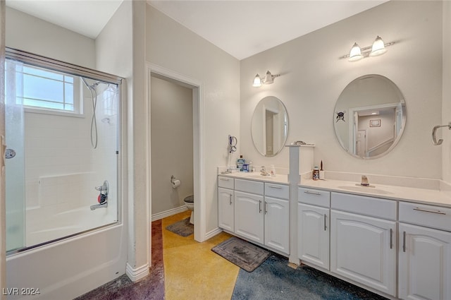 full bathroom with bath / shower combo with glass door, toilet, and dual bowl vanity