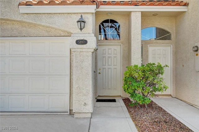 doorway to property featuring a garage, a tiled roof, and stucco siding