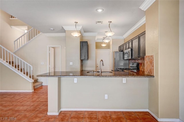 kitchen featuring stainless steel appliances, a sink, dark brown cabinets, dark stone counters, and a peninsula