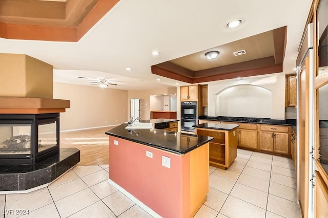 kitchen featuring a raised ceiling, ceiling fan, sink, light tile patterned floors, and an island with sink