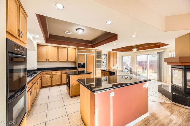 kitchen with a center island, black appliances, a raised ceiling, sink, and ceiling fan