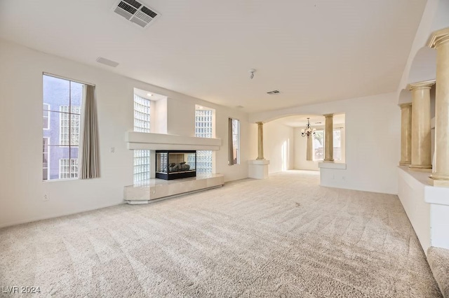 unfurnished living room featuring plenty of natural light, carpet floors, a fireplace, and decorative columns