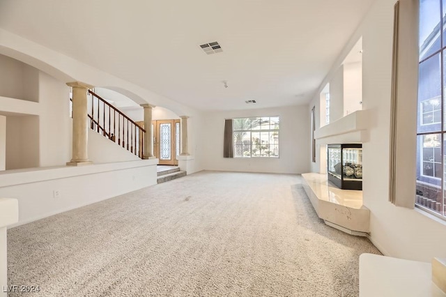 unfurnished living room with decorative columns, carpet flooring, and a multi sided fireplace