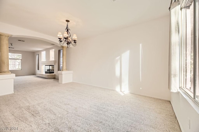 unfurnished living room with carpet, a multi sided fireplace, ornate columns, and a chandelier