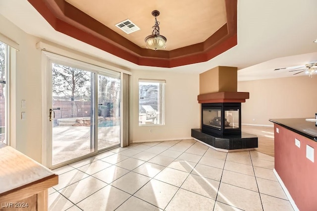 interior space with a tray ceiling, a tiled fireplace, ceiling fan, and light tile patterned flooring