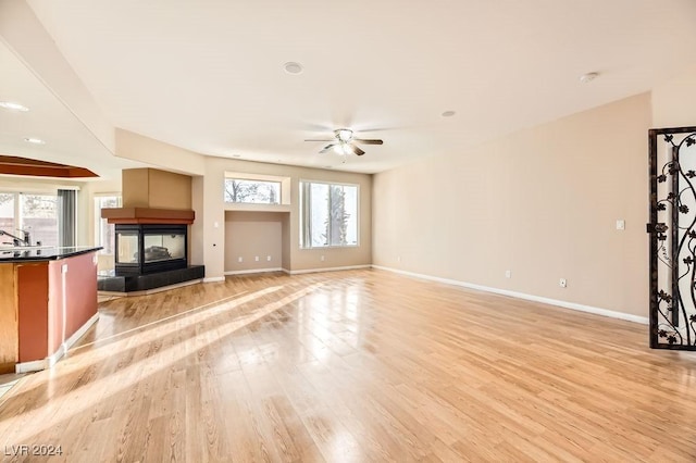 unfurnished living room featuring a multi sided fireplace, ceiling fan, plenty of natural light, and light hardwood / wood-style floors