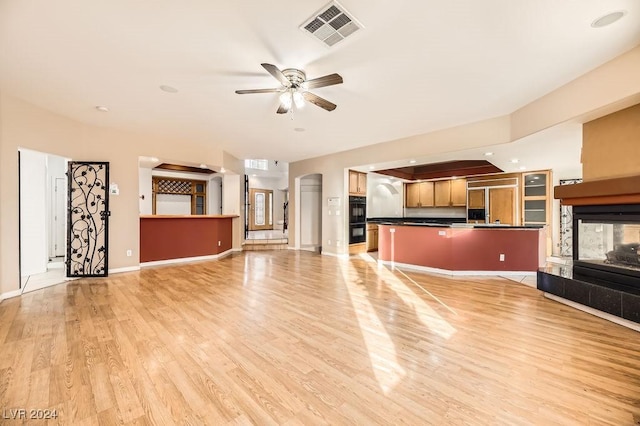 unfurnished living room with a multi sided fireplace, light wood-type flooring, and ceiling fan