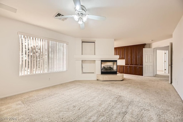 unfurnished living room with a multi sided fireplace, ceiling fan, and light carpet