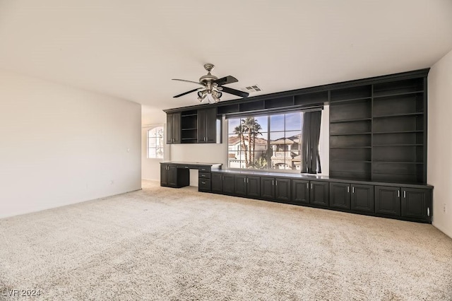 unfurnished living room with built in shelves, carpet floors, and ceiling fan