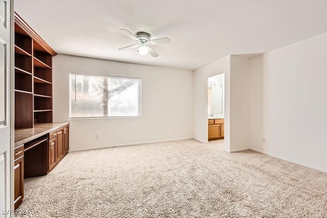 unfurnished living room with ceiling fan, built in desk, and light carpet