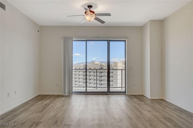 unfurnished room with a ceiling fan, a view of city, baseboards, and wood finished floors