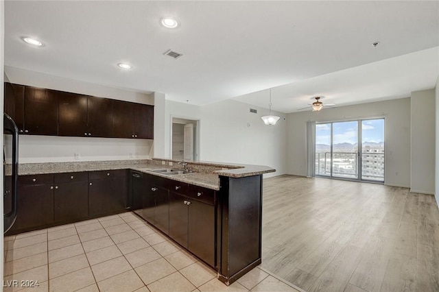 kitchen with a peninsula, a sink, open floor plan, dark brown cabinets, and light stone countertops