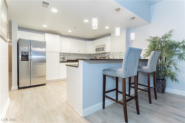 kitchen with white cabinetry, backsplash, stainless steel appliances, kitchen peninsula, and light hardwood / wood-style floors