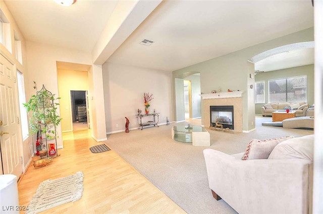 living area featuring baseboards, visible vents, arched walkways, a tiled fireplace, and wood finished floors