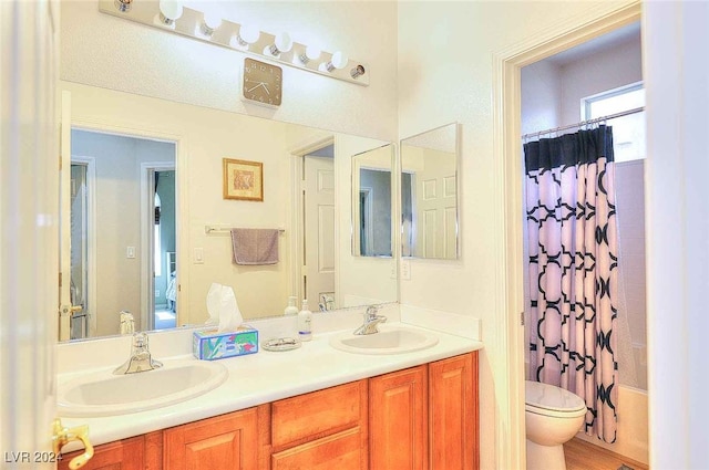 bathroom featuring toilet, double vanity, shower / bath combo with shower curtain, and a sink