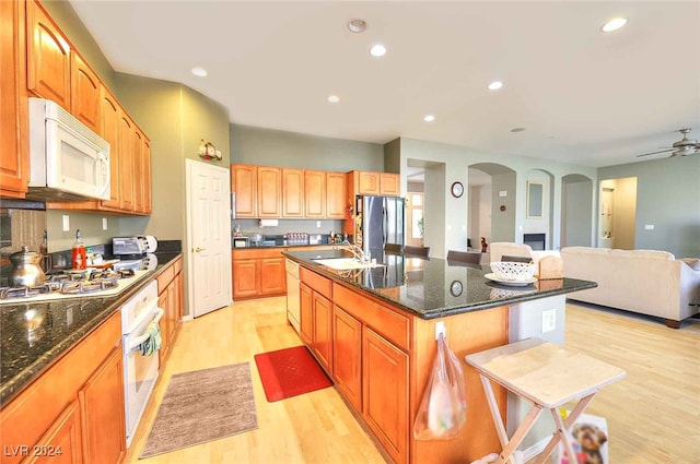 kitchen featuring a breakfast bar, arched walkways, open floor plan, a kitchen island with sink, and white appliances