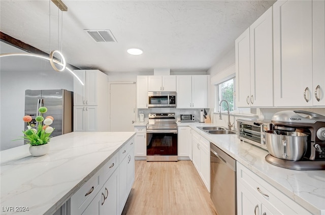 kitchen featuring stainless steel appliances, light hardwood / wood-style floors, white cabinetry, sink, and pendant lighting