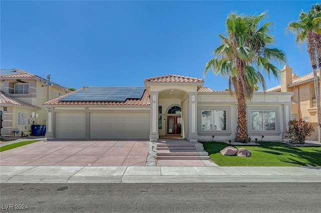 mediterranean / spanish-style home featuring a garage, solar panels, and a front lawn