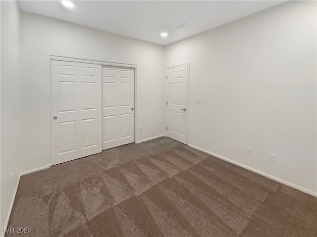 unfurnished bedroom with dark colored carpet and a closet