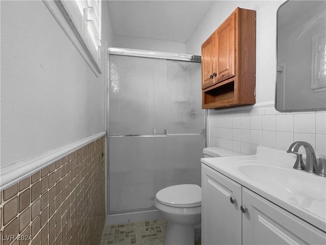 bathroom featuring toilet, a shower with shower door, tile walls, and vanity