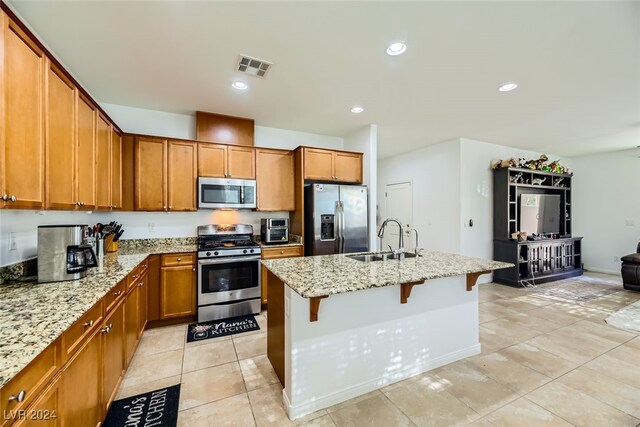 kitchen featuring light stone counters, sink, a breakfast bar area, a center island with sink, and stainless steel appliances