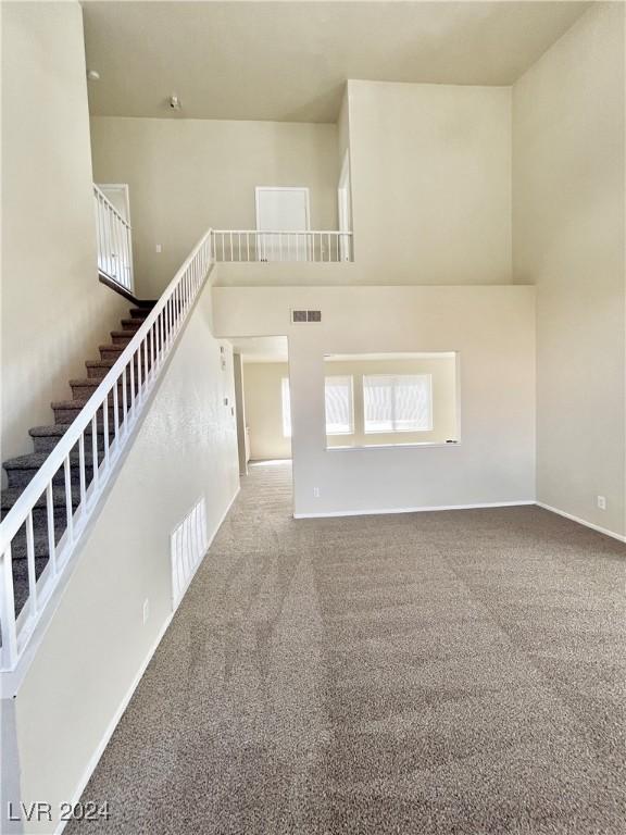 interior space featuring carpet, visible vents, a high ceiling, and stairs