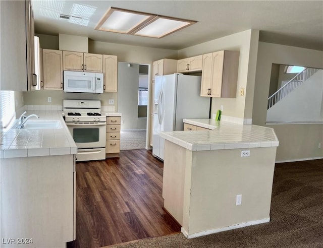 kitchen featuring a peninsula, white appliances, a sink, and tile counters