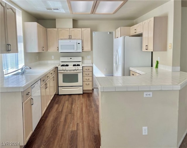 kitchen featuring white appliances, tile counters, dark wood-style flooring, a peninsula, and a sink