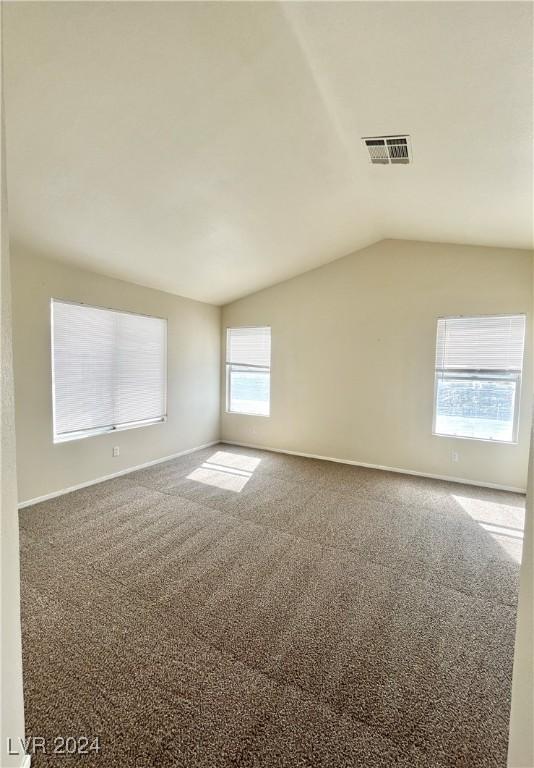 carpeted empty room featuring lofted ceiling, visible vents, and baseboards